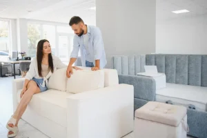 A man and woman sit together on a couch in a furniture store, examining the fabric and style of the furniture.