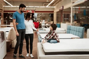 A family examines various mattresses in a store, discussing options and comparing features together.